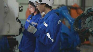 fábrica engenheiro mulher inspecionando em máquina com inteligente tábua. trabalhador trabalho às máquina robô braço. a Soldagem máquina com uma controlo remoto sistema dentro a industrial fábrica. artificial inteligência conceito. video