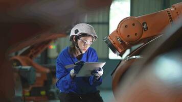 fábrica engenheiro mulher inspecionando em máquina com inteligente tábua. mulher caminhando às máquina robô braço. a Soldagem máquina com uma controlo remoto sistema dentro a industrial fábrica. artificial inteligência conceito. video