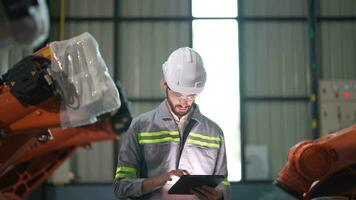 fabbrica uomo ingegnere ispezionando su macchina con inteligente tavoletta. lavoratore lavori a pesante macchina robot braccio. artificiale intelligenza concetto. specialista lavoratore Lavorando a altezza tecnologia industria. video