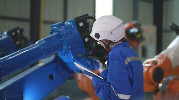 usine ingénieur femme inspecter sur machine avec intelligent tablette. ouvrier travaux à machine robot bras. le soudage machine avec une éloigné système dans un industriel usine. artificiel intelligence concept. video