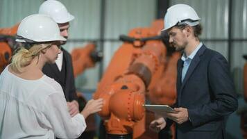 bedrijf ingenieurs ontmoeten en controleren controle zwaar machine robot arm. verschillend team van industrieel robotica ingenieurs verzameld in de omgeving van machine. professioneel machinerie operator gebruik industrieel digitaal tablet. video