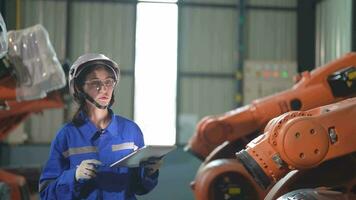 fabrik ingenjör kvinna inspekterande på maskin med smart läsplatta. kvinna gående på maskin robot ärm. de svetsning maskin med en avlägsen systemet i ett industriell fabrik. artificiell intelligens begrepp. video