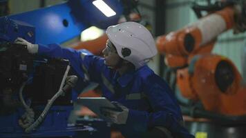 usine ingénieur femme inspecter sur machine avec intelligent tablette. ouvrier travaux à machine robot bras. le soudage machine avec une éloigné système dans un industriel usine. artificiel intelligence concept. video