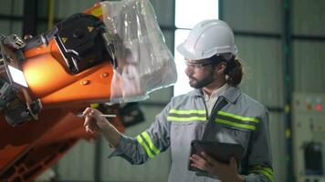 fabriek Mens ingenieur inspecteren Aan machine met slim tablet. arbeider werken Bij zwaar machine robot arm. kunstmatig intelligentie- concept. specialist arbeider werken Bij hoogte technologie industrie. video