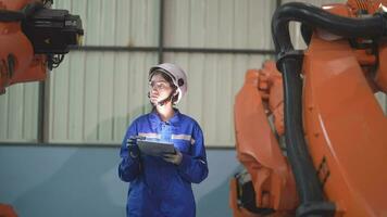 fabriek ingenieur vrouw inspecteren Aan machine met slim tablet. vrouw wandelen Bij machine robot arm. de lassen machine met een afgelegen systeem in een industrieel fabriek. kunstmatig intelligentie- concept. video