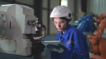 usine ingénieur femme inspecter sur machine avec intelligent tablette. ouvrier travaux à machine robot bras. le soudage machine avec une éloigné système dans un industriel usine. artificiel intelligence concept. video