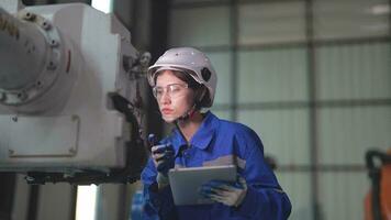 fabriek ingenieur vrouw inspecteren Aan machine met slim tablet. arbeider werken Bij machine robot arm. de lassen machine met een afgelegen systeem in een industrieel fabriek. kunstmatig intelligentie- concept. video