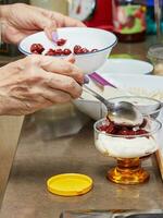 Chef preparing special dessert with fresh cream, cherry, cookies and nuts in a glass photo