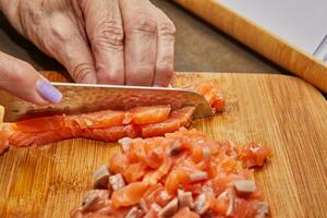 Chef's Hands Cutting Fresh Salmon Fillet with Knife on Wooden Cutting Board in Kitchen photo