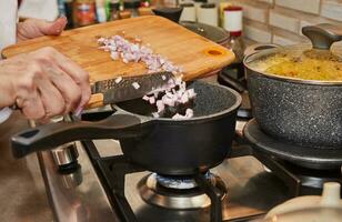 de cerca de un del chef manos lanzamiento Fresco chalotes dentro un pan en un gas cocina. concepto de hogar Cocinando y culinario preparación en el cocina foto