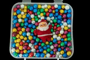 Santa Claus with pile of small colorful thermocol balls in plastic box isolated on black background. photo