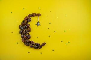 Ramadan holiday concept, on a yellow background of dates in the form of a moon with shiny stars. High quality photo