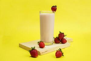 a glass of milk with strawberry garnish on cut board isolated yellow background photo