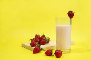 a glass of milk with strawberry garnish on cut board isolated yellow background photo