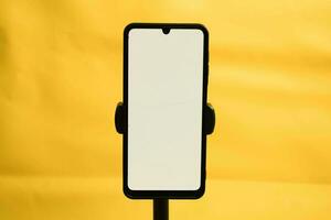 Portrait phone with white screen fixed to tripod on yellow background, for mockup design. photo