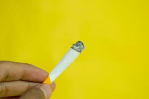 un hombre mano sostiene un hecho a mano cigarrillo en amarillo antecedentes foto