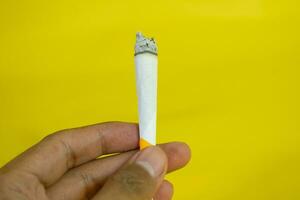 un hombre mano sostiene un hecho a mano cigarrillo en amarillo antecedentes foto