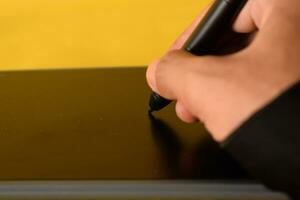 The hand wearing glove draws on a graphics tablet. Freelance, designer, Illustrator on yellow background photo