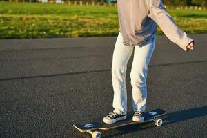 recortado Disparo de piernas en longboard patinador niña montando su patineta en calle. hembra adolescente en crucero foto