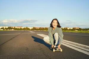 Portrait of carefree, happy asian girl skating, riding skateboard and laughing, enjoying sunny day photo