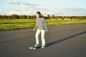 aficiones y estilo de vida. joven mujer montando patineta. patinador niña disfrutando crucero en longboard en soleado día al aire libre foto