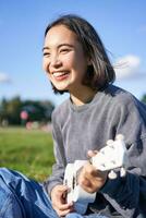 Vertical shot of happy korean girl sitting in park, learning how to play ukulele, singing and relaxing photo