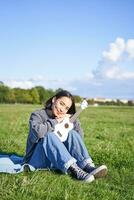 Romantic asian girl sitting with ukulele guitar in park and smiling, relaxing after university, enjoying day off on fresh air photo