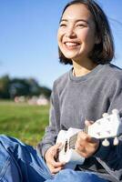 vertical Disparo de contento coreano niña sentado en parque, aprendizaje cómo a jugar ukelele, canto y relajante foto