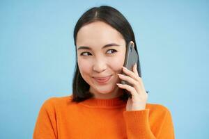 tecnología concepto. cerca arriba de sonriente asiático mujer negociaciones en móvil teléfono, teniendo conversacion en Teléfono móvil, azul antecedentes foto