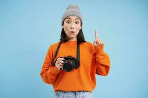 apasionado asiático niña fotógrafo, tomando imágenes en su digital cámara, capturar momentos al aire libre, disparo fotos, azul antecedentes foto
