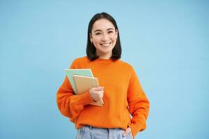 Education concept. Young smiling asian woman with notebooks, looking happy at camera, student going to uni photo