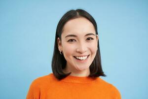 Close up portrait of beautiful korean woman with healthy smile, natural clear facial skin, stands over blue background photo