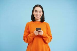 Girl with smartphone in hands smiling, using mobile application on her phone, sending message or order something online, blue background photo