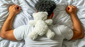 ai generado joven hombre dormido en cama con un osito de peluche oso en su espalda. generativo ai foto