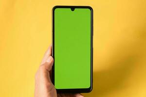 hand holding modern mobile phone green screen isolated on yellow background photo