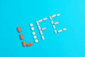 Life word from Colorful Medicine Pills isolated on blue background, supplement, vitamin, colorful photo