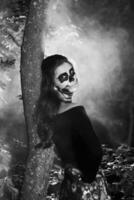 Portrait of young woman with scared halloween makeup in forrest. halloween make up sugar skull beautiful model with perfect hairstyle. Devil girl concept. photo