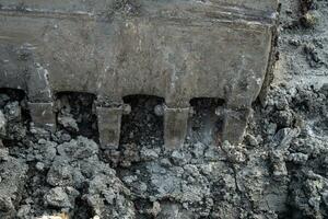 Closeup dirty bucket of backhoe working at construction site. Bucket teeth of backhoe digging soil. Crawler excavator digging on soil. Excavating machine. Earthmoving machine. Excavation vehicle. photo