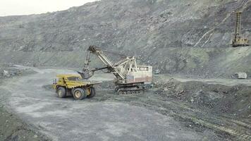 Excavator and dump truck while loading stone ore in a grey quarry, mining industry. Stock. Heavy mining excavator loads rock ore into a dump-body large mining truck, quarry equipment. photo