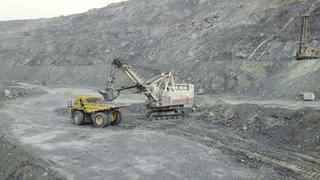 excavador y tugurio camión mientras cargando Roca mineral en un gris cantera, minería industria. existencias. pesado minería excavador cargas rock mineral dentro un cuerpo volcado grande minería camión, cantera equipo. foto