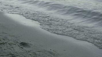 suave ola de el mar en el arenoso playa. de cerca detalle de el espumoso mar olas Lavado en tierra a el playa foto