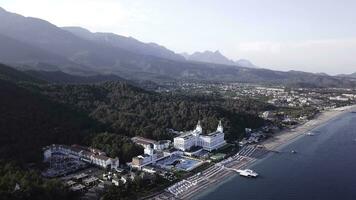 Video. Aerial view of Hotel on sea shore and mountains covered with green forest, trees with blue sky at sunrise. Video. Aerial view on seashore with luxury Hotel with forest and mountains background photo