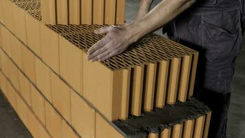 Close up of a worker standing at the unfinished red brick wall and drawing a line with his hand for further actions. Stock footage. Detail of worker and layers of bricks. photo