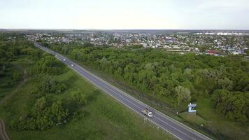 Top view of highway passing through village with forest. Clip. Track with passing cars on background of village with green forest and horizon with sky photo