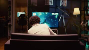 giocatore nel accogliente vivente camera gode gioco con navicella spaziale tiro laser flussi utilizzando mirino copertura per colpire nemici. uomo giochi su consolle sistema con raggio tracciato grafica e alto fps, Ingrandisci su tiro video