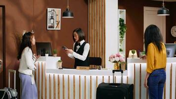 Asian traveler paying for hotel room during check in process, choosing pos terminal payment with credit card. Young woman with luggage making electronic transaction for accommodation. video