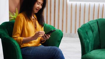 Hotel guest waiting for check in process at hotel, using phone to scroll on social media and pass time. Asian woman arriving early at five star resort, relaxing after long flight. video