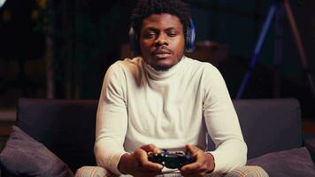 Portrait of BIPOC man wearing headphones and playing intense online videogame, spamming buttons on controller. Gamer participating in internet esports competition, playing on gaming console, close up video
