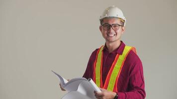 joven Asia sonriente hermoso ingeniero en blanco casco posando con planos mirando a cámara aislado en blanco antecedentes. video