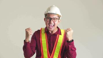 Handsome young asian engineer wearing orange vest and helmet over isolated white background.Celebrating surprised and amazed for success with arms raised. Winner concept. video